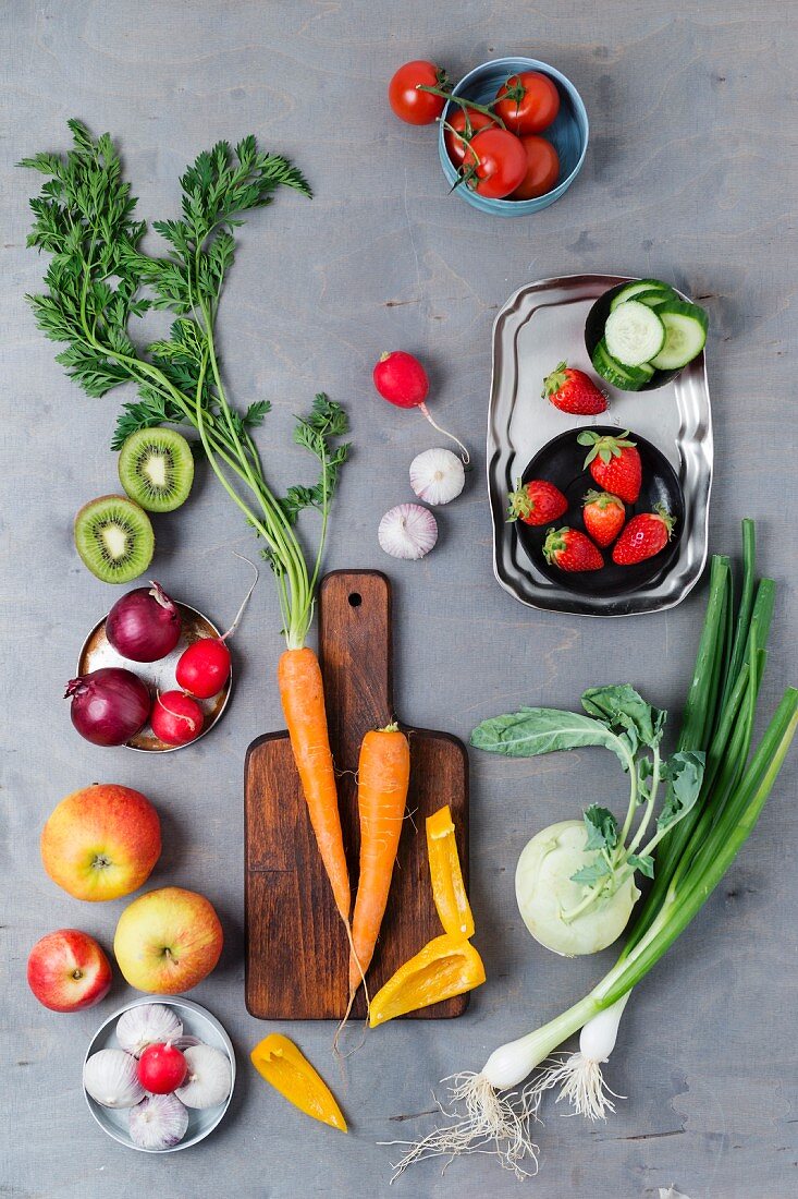 An arrangement of spring onions, garlic, apples, tomatoes, peppers, carrots, kiwi, radishes, strawberries and kohlrabi