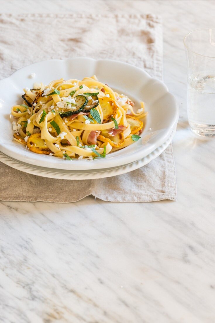 Fresh homamade tagliatelle with yellow and green courgette, bacon and goat cheese