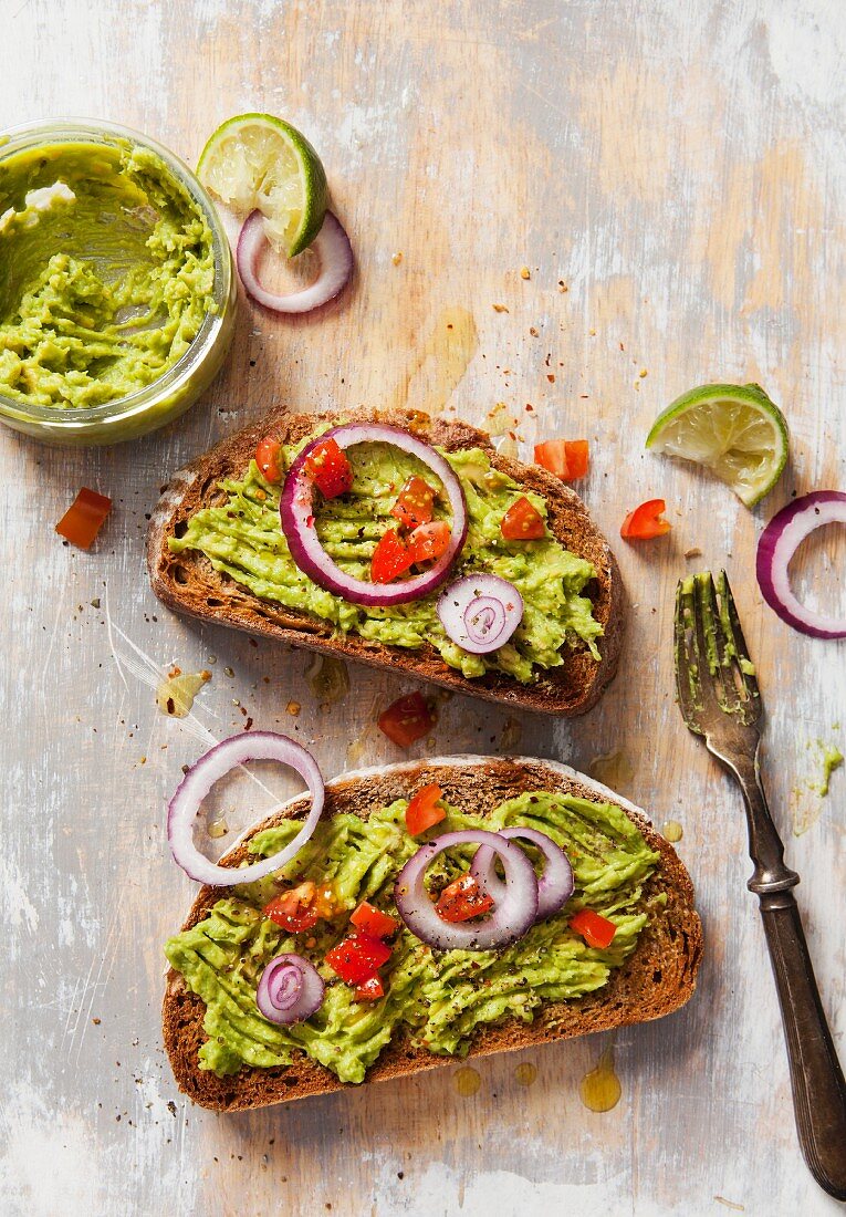 Two slices of avocado on toasted bread garnished with fresh diced tomato and sliced red onion