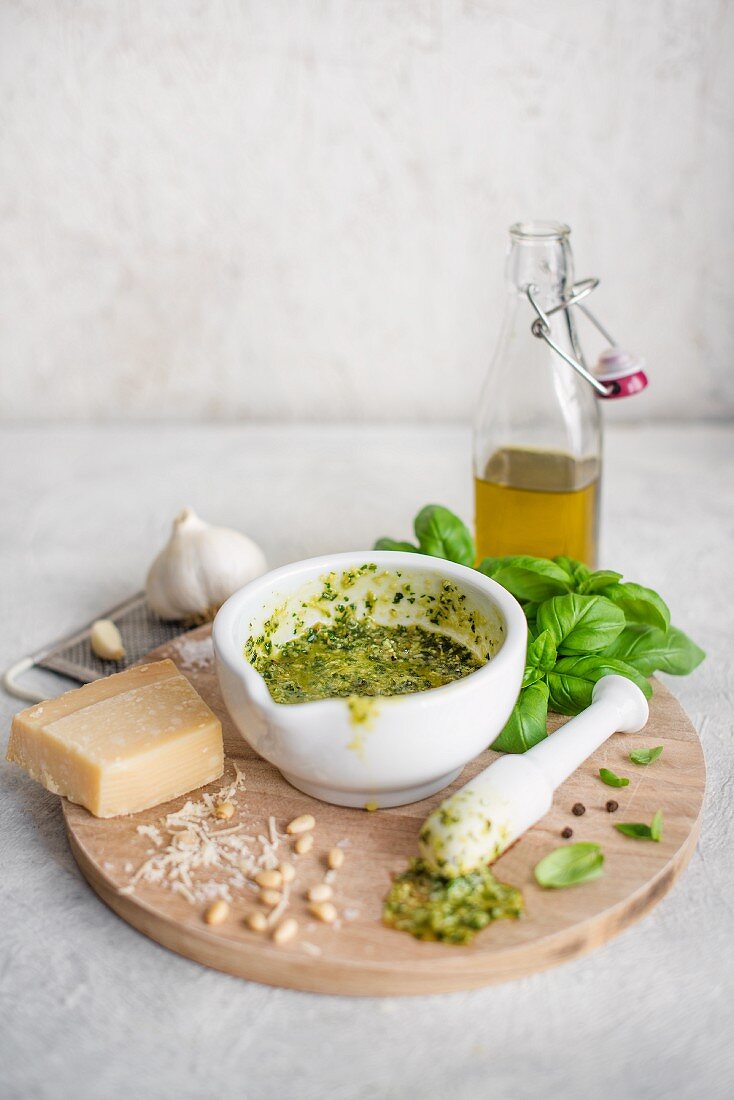 Basil pesto in mortar surrounded by the ingredients