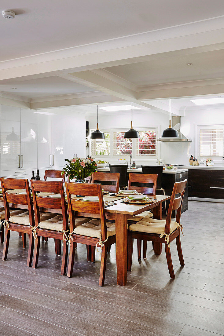 Dining area with wooden table and chairs, in the background open kitchen with porcelain floor tiles in a wood look