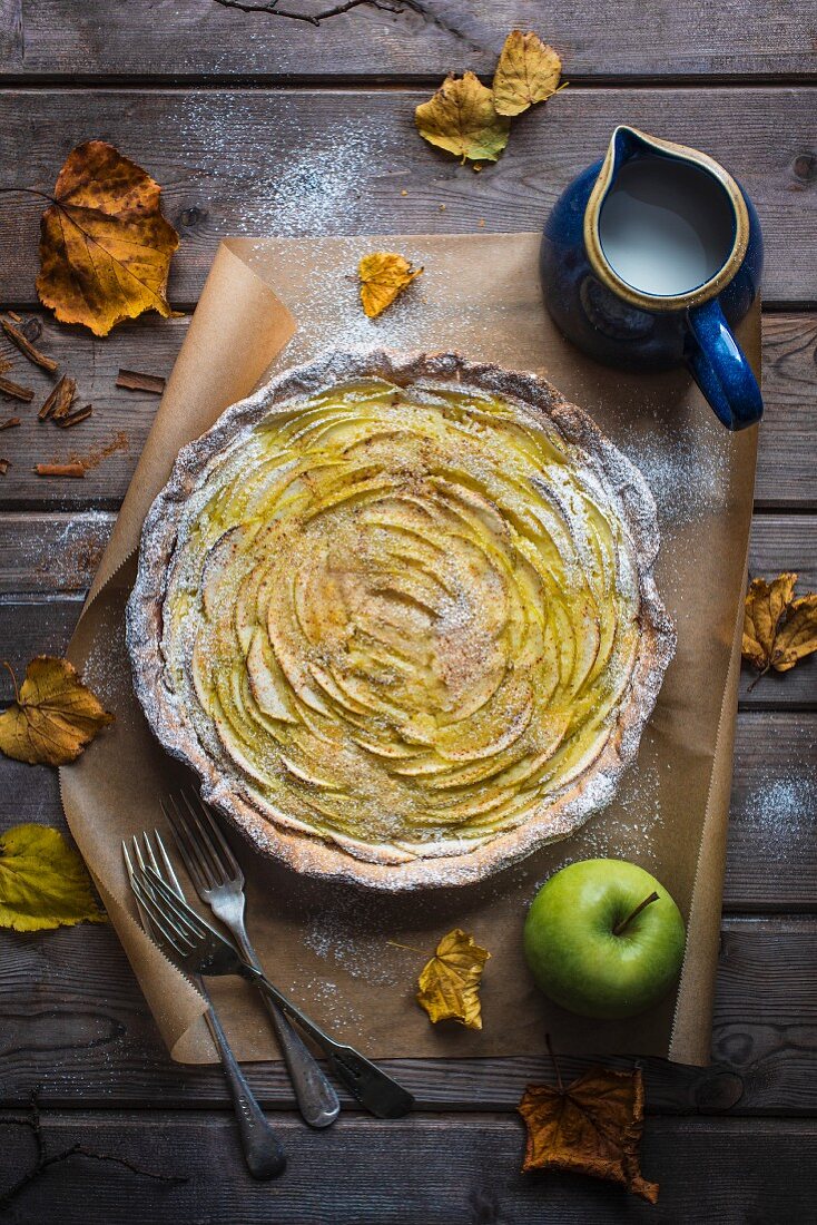 Apple and almond frangipane tart with an autumnal leaves and a jug of cream, view from above