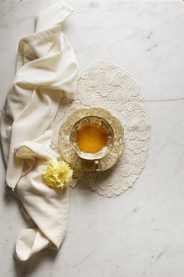Grüner Tee in Teetasse auf Spitzendeckchen daneben Serviette und Blüte