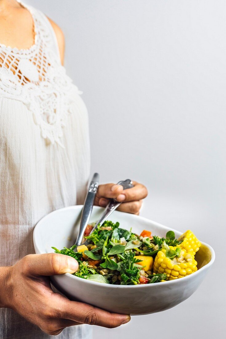 A woman wearing a white lace top holding a bowl of lentil salad in her hands