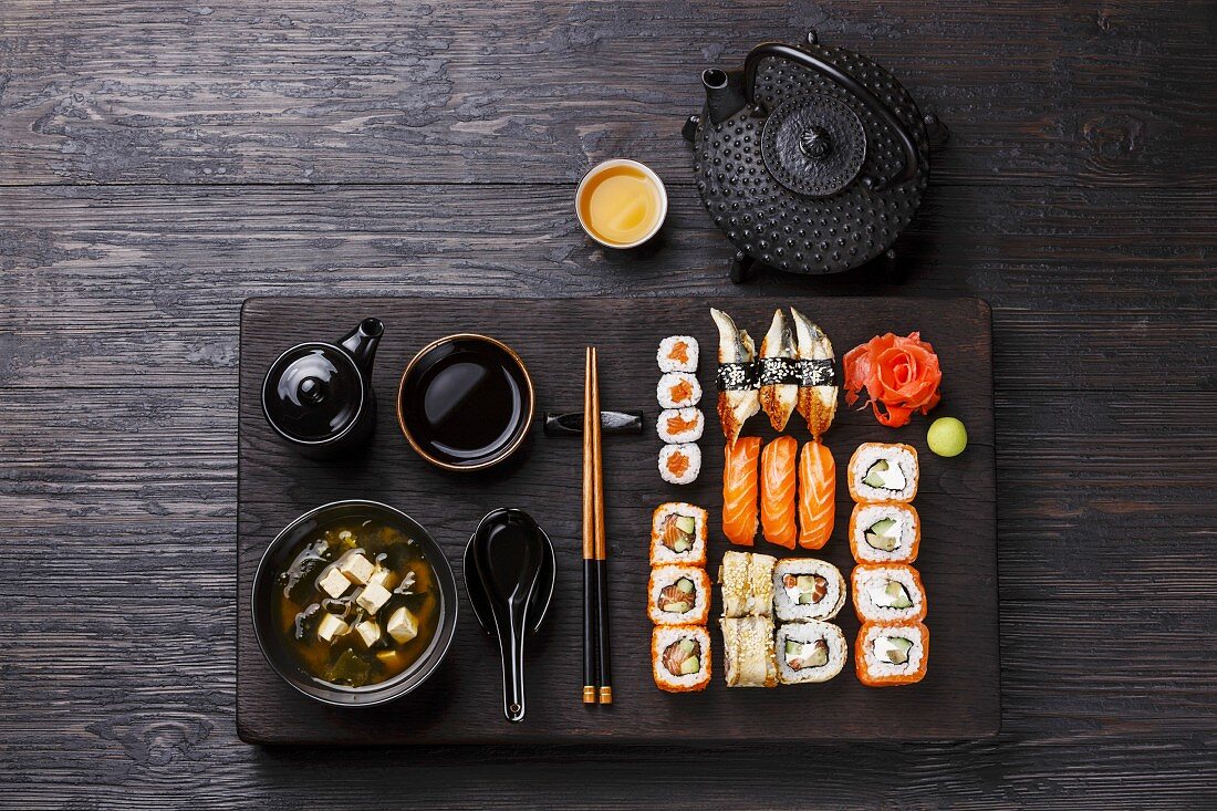Sushi Set nigiri and sushi rolls and Miso Soup with tofu on wooden serving board block on black background