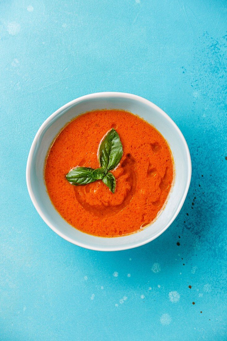 Tomaten-Gazpacho in Schälchen vor blauem Hintergrund (Aufsicht)