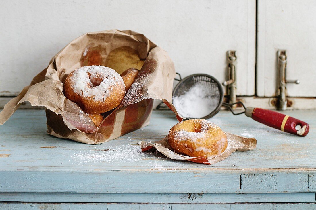 Homemade donuts with sugar powder from paper bag served with vintage sieve on blue wooden table