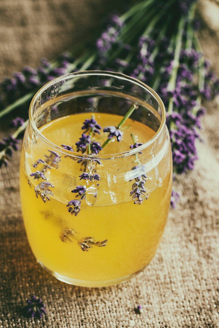 Organic raw honey in glass jar flavored with lavender flowers, standing on table with sackcloth