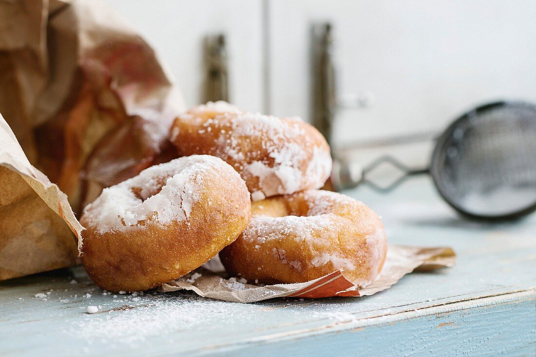 Homemade donuts with sugar powder from paper bag served with vintage sieve on blue wooden table
