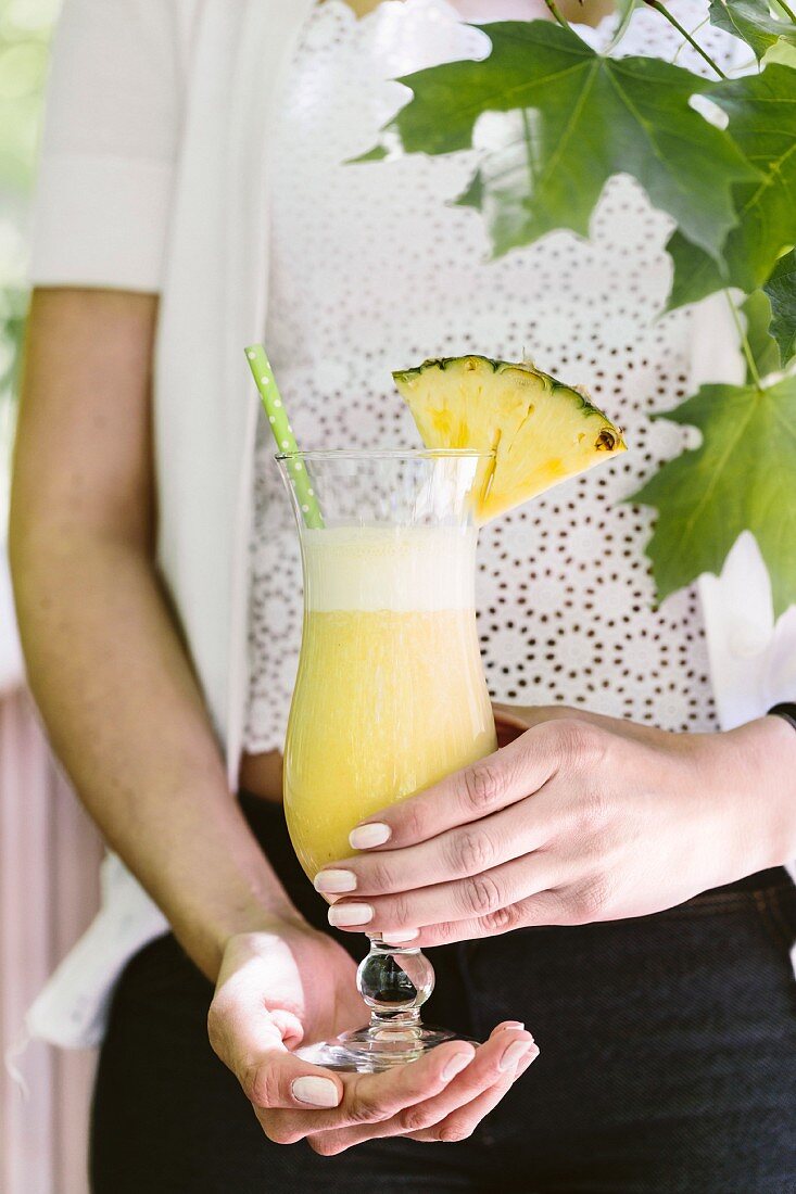 A woman holds a pina colada cocktail