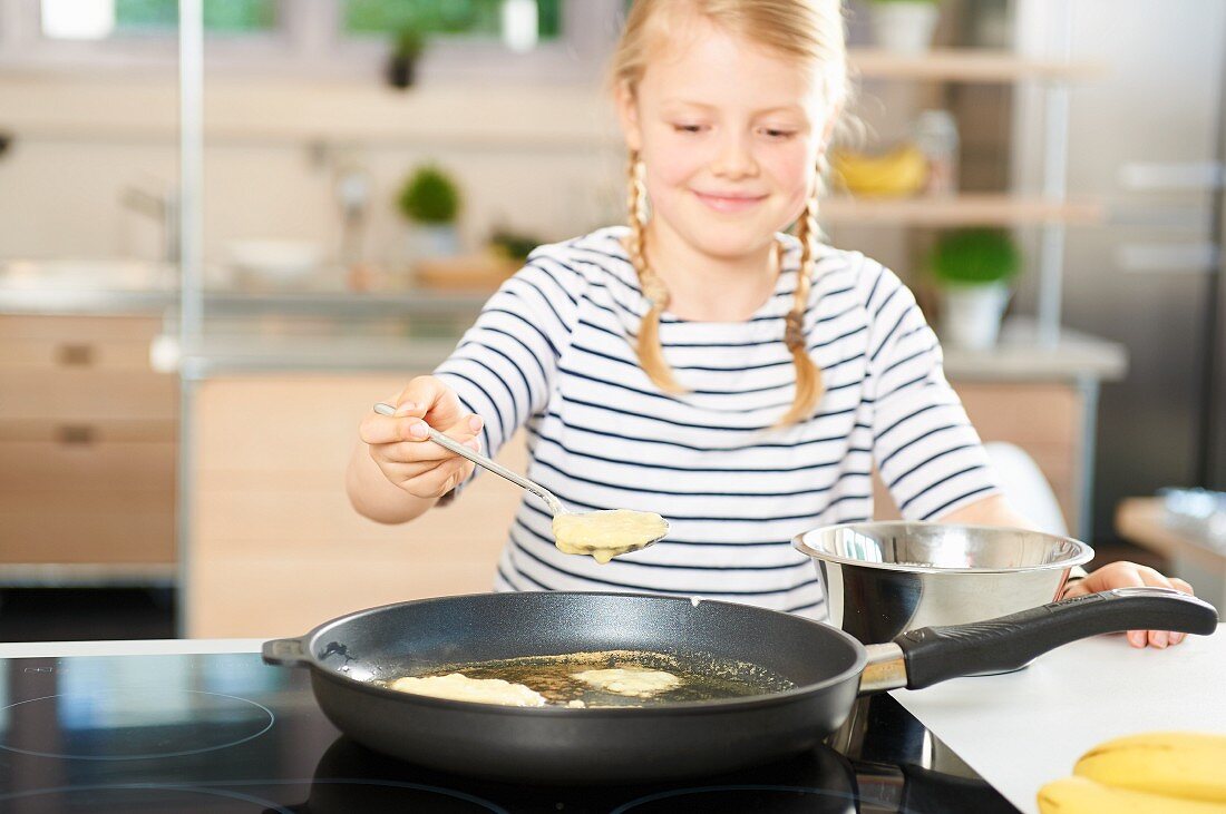 Mädchen brät Bananen-Pancakes in einer Pfanne