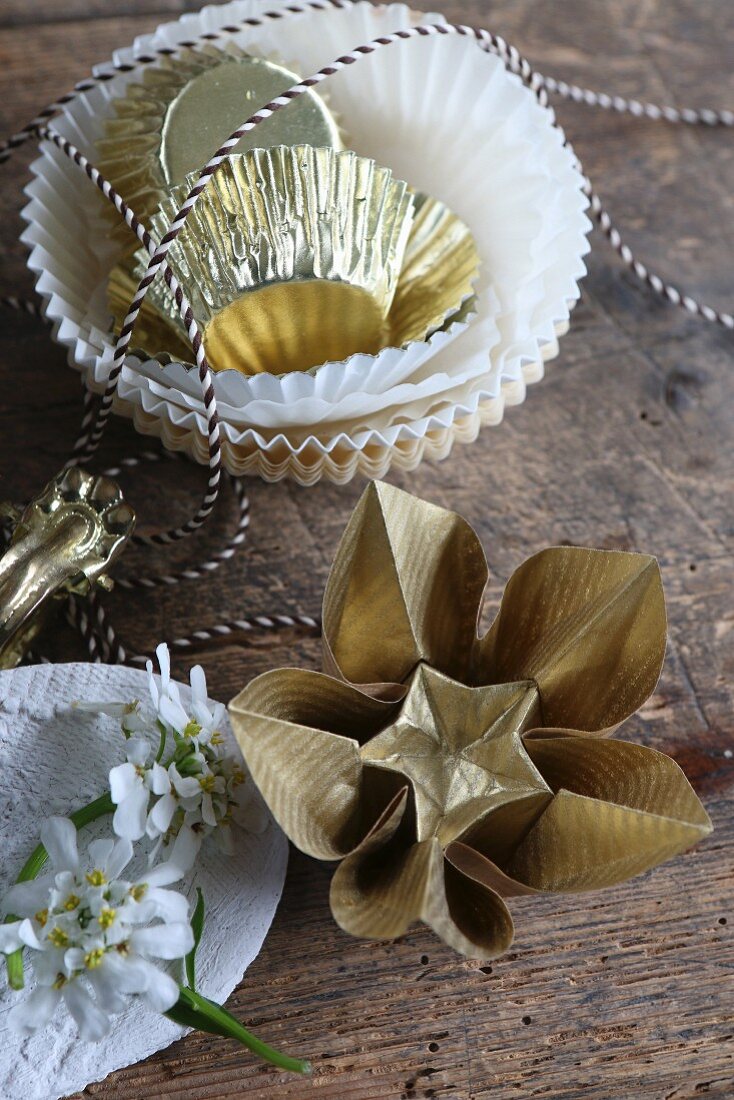 Gold origami flowers next to paper cake cases and bakers' string