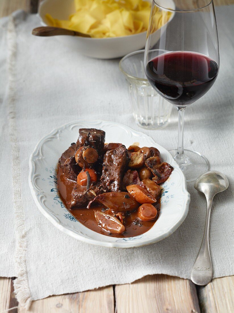 Boeuf Bourguignon mit Glas Rotwein und Bandnudeln