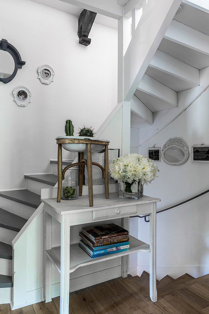 Books and flower arrangement on white table at foot of staircase