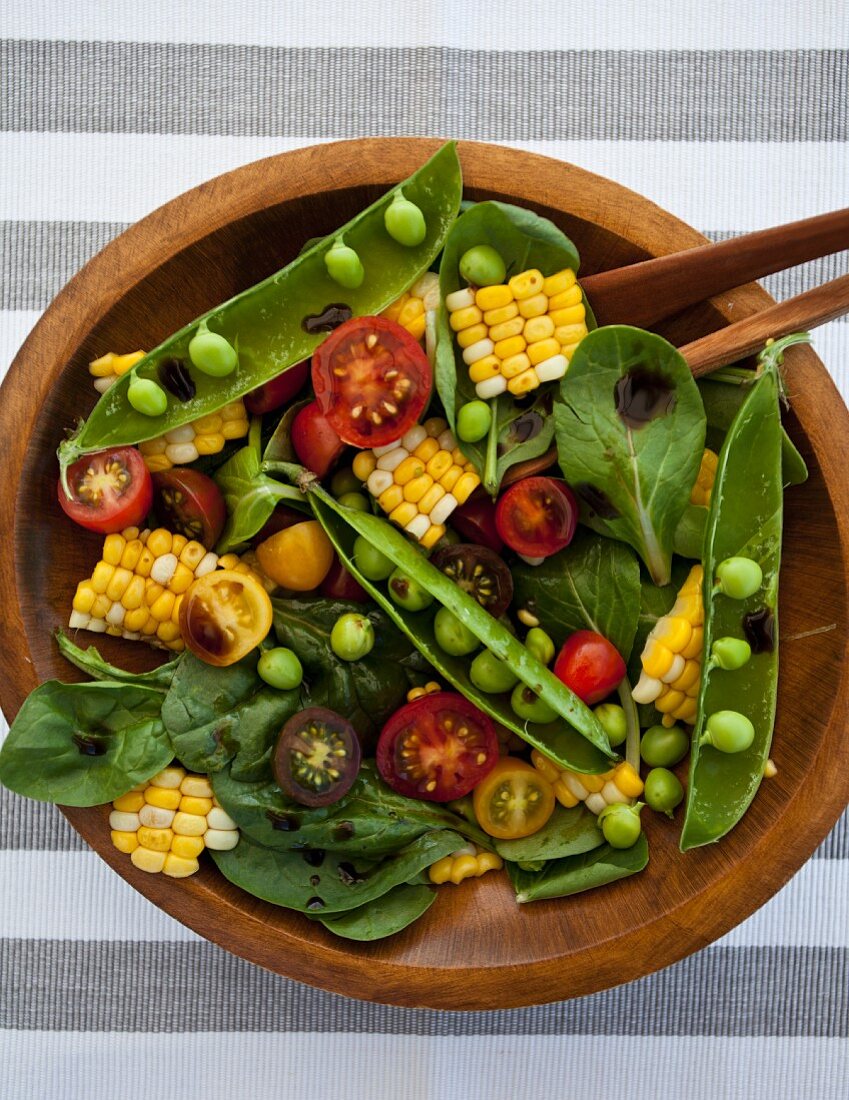 A spinach salad with corn, heirloom tomatoes and green peas, with balsamic vinegar drizzled on top