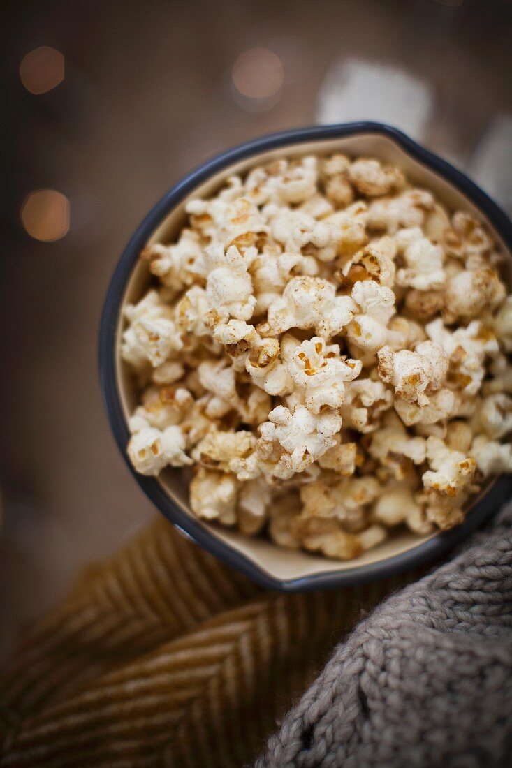 Vanilla and cinnamon pop corn in an annamel pan with blankets against a dark background with fairy lights