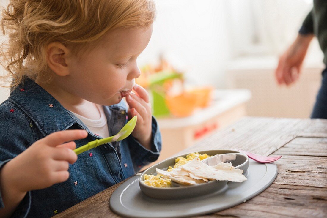 Caucasian girl eating with fingers and spoon