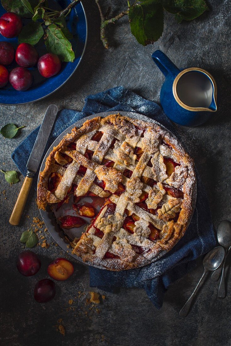 Plum tart, sliced removed with fresh plums and a jug of cream