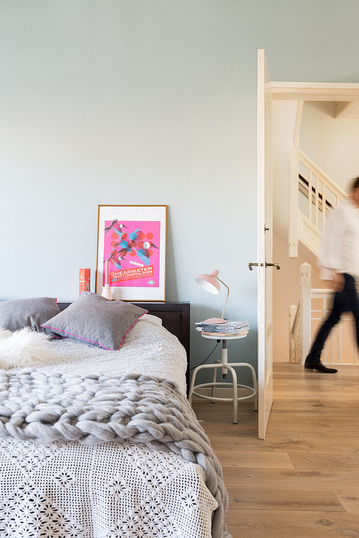 Spitzendecke und grobe Strickdecke auf dem Bett vor grauer Wand