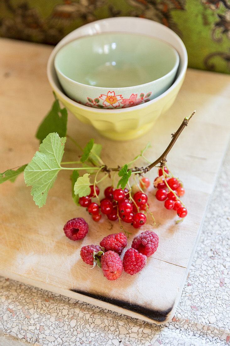 Zweig mit Johannisbeeren und Himbeeren auf einem Holzbrett