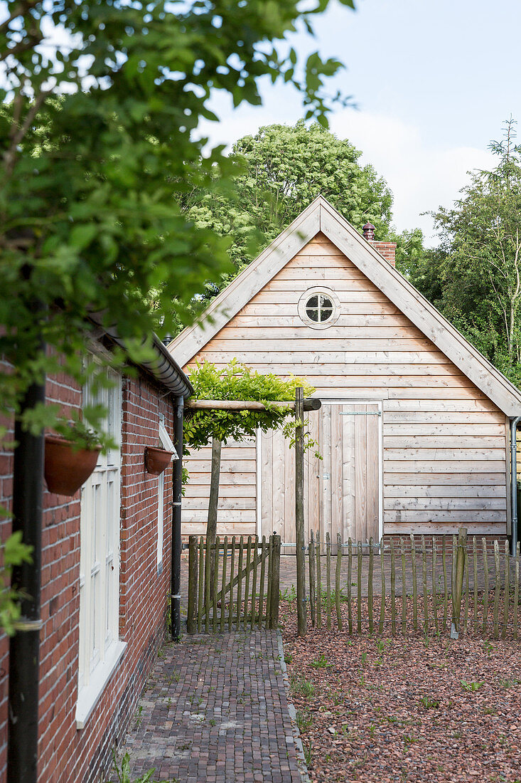 Path running alongside brick wall leading to wooden cabin with paling fence