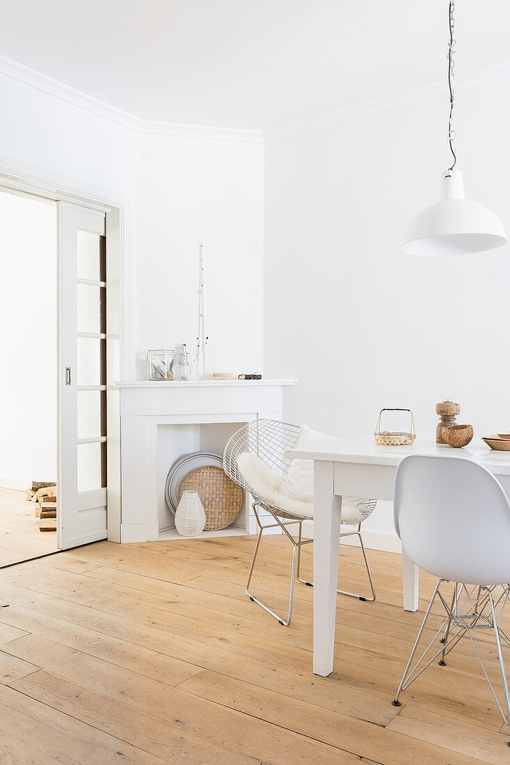 White dining area: dining table and classic chairs on wooden floorboards with disused fireplace in corner