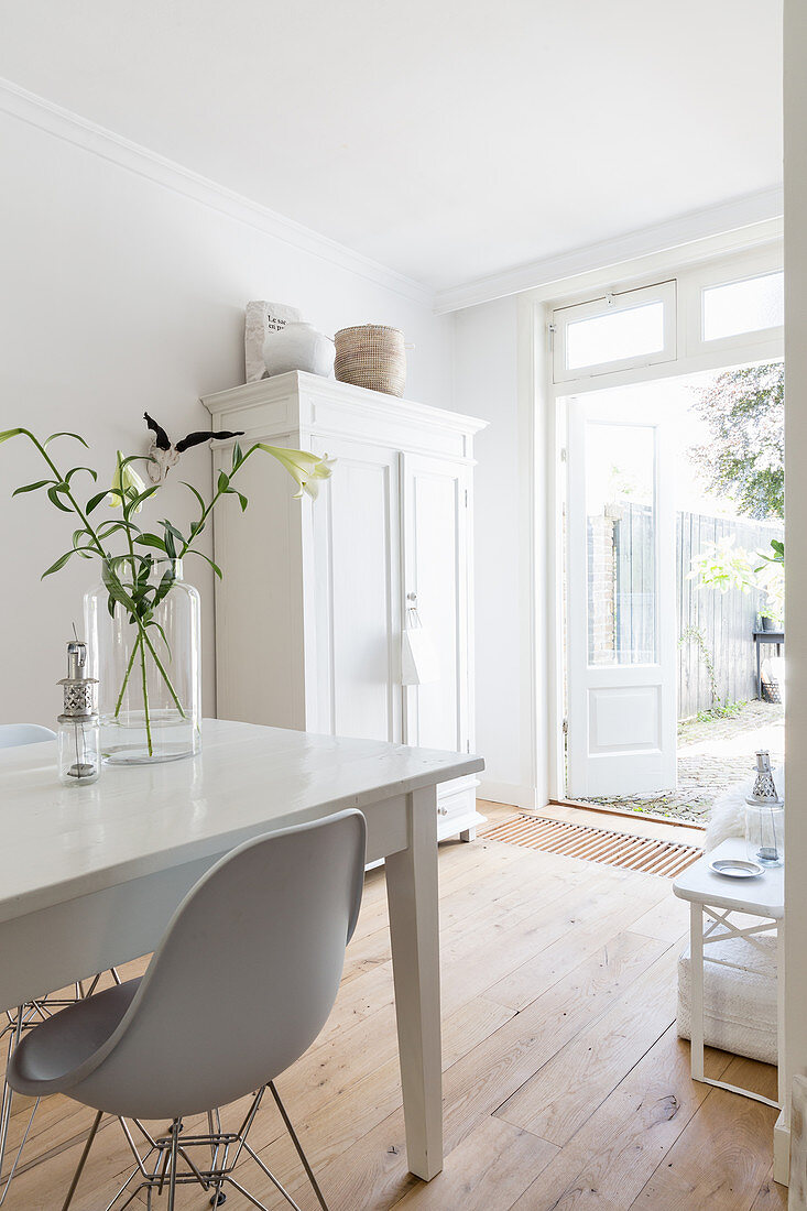 White dining table and classic chairs on wooden floor in front of white cupboard next to terrace doors