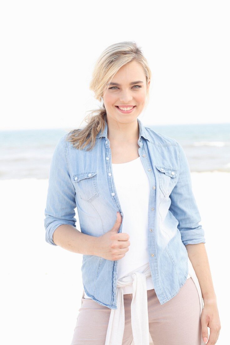 A young blonde woman on a beach wearing a denim shirt