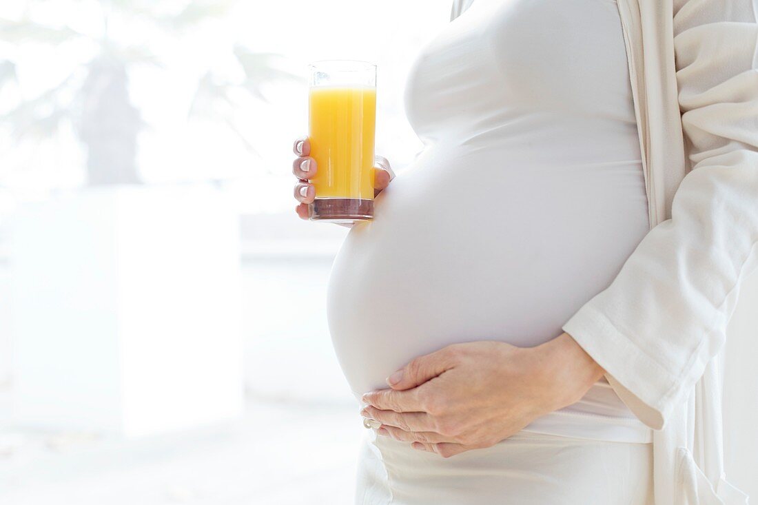 Pregnant woman touching tummy with juice