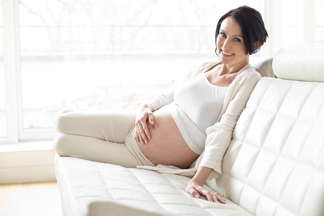 Pregnant woman on sofa touching tummy