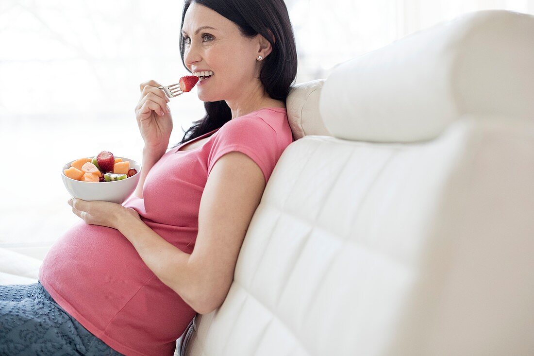 Pregnant woman on sofa eating fresh fruit