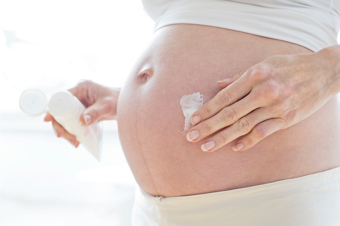 Pregnant woman applying moisturiser to her tummy