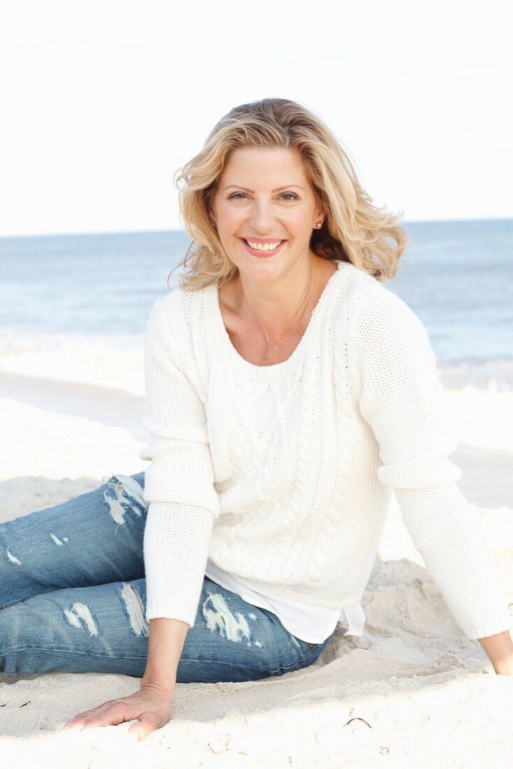 A blonde woman wearing a white jumper and jeans