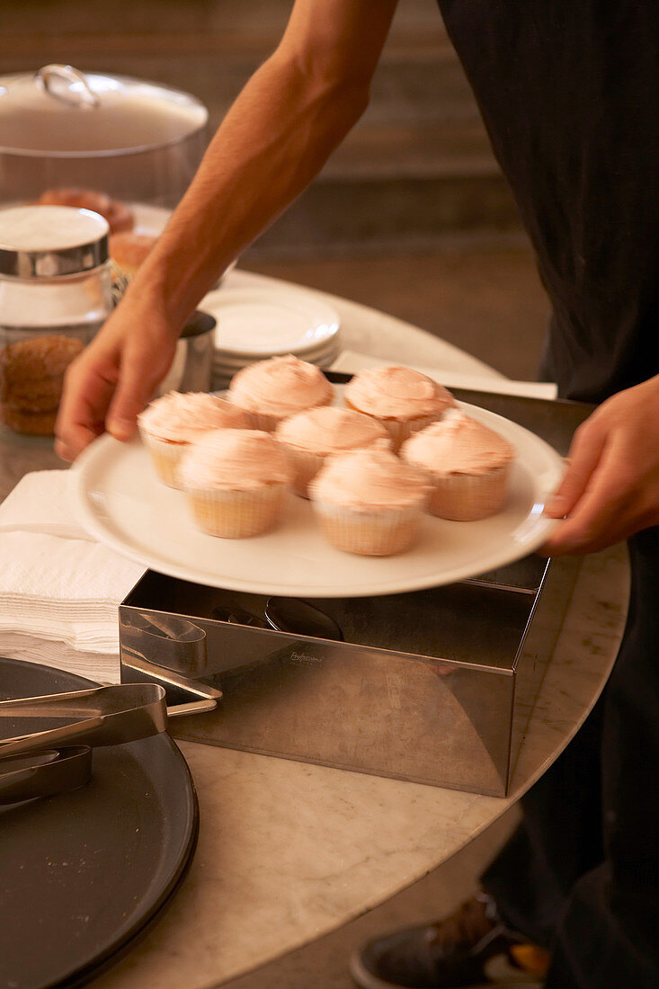 Ein Teller Muffins mit Cremehaube werden auf Tisch gestellt.
