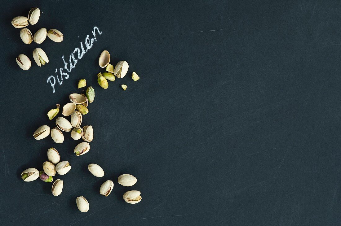 Pistachios, whole and hulled, arranged around the German word for pistachios written in chalk on a blackboard