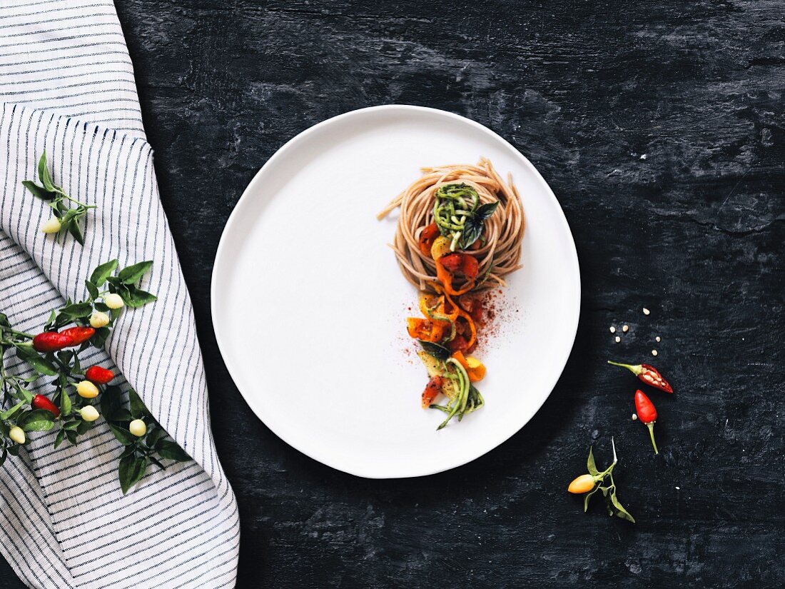 Whole-wheat fettucine with brightly coloured chillis on a plate and a black background