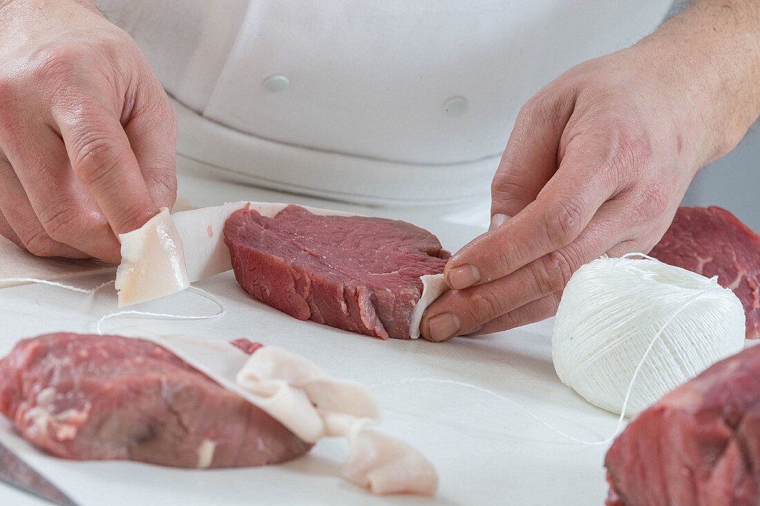 A chef wrapping a fillet steak in bacon