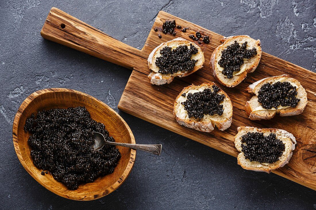 Schwarzer Kaviar in Holzschale und auf Weissbrotscheiben
