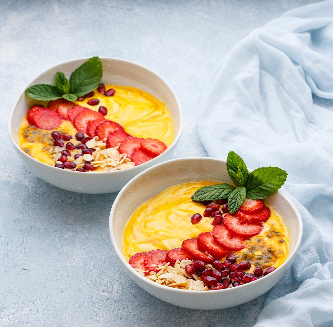 Mango and passion fruit smoothie bowls topped with strawberries and almonds