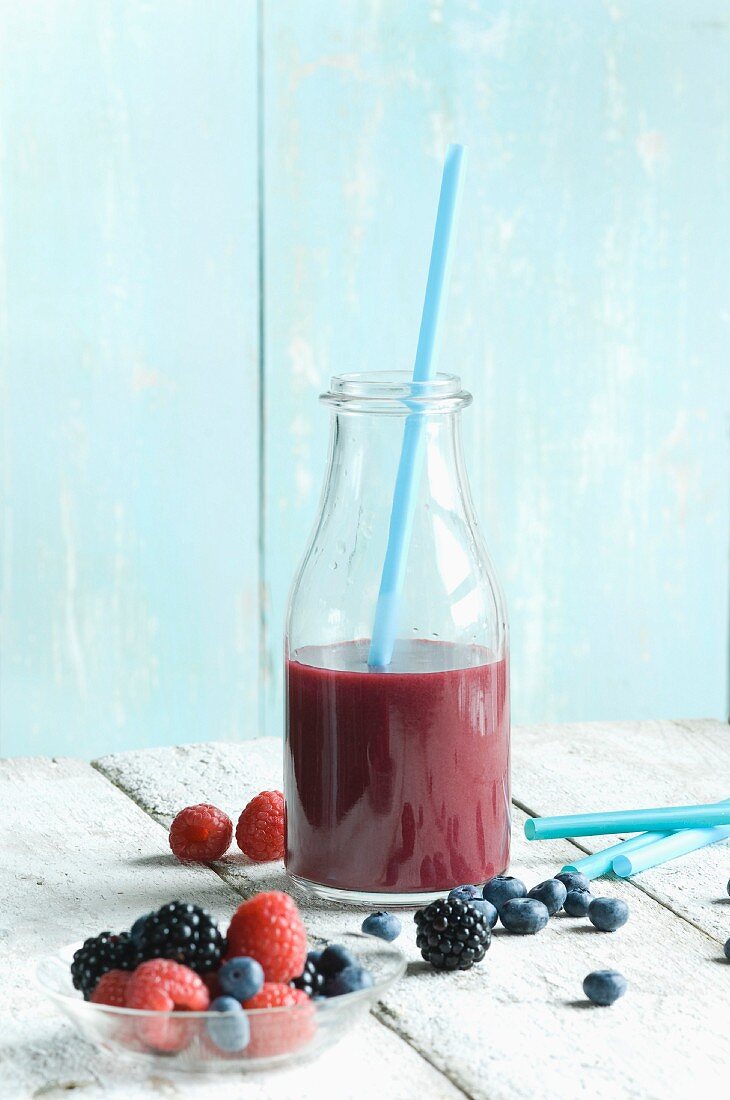 A blueberry smoothie with raspberries, blackberries and blueberries on the table next to it