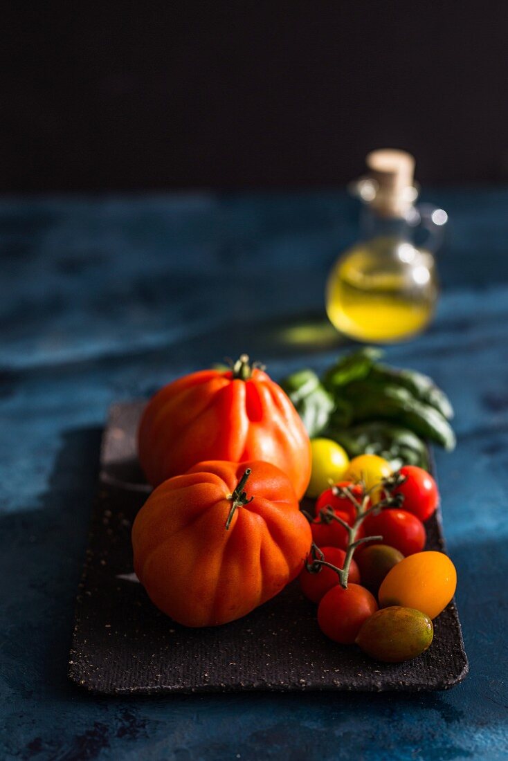 Verschiedene Tomatensorten auf Tablett, dahinter Olivenöl