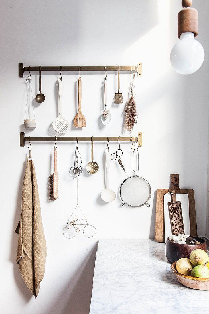 Utensils hung from hook rails in kitchen with wooden cabinets