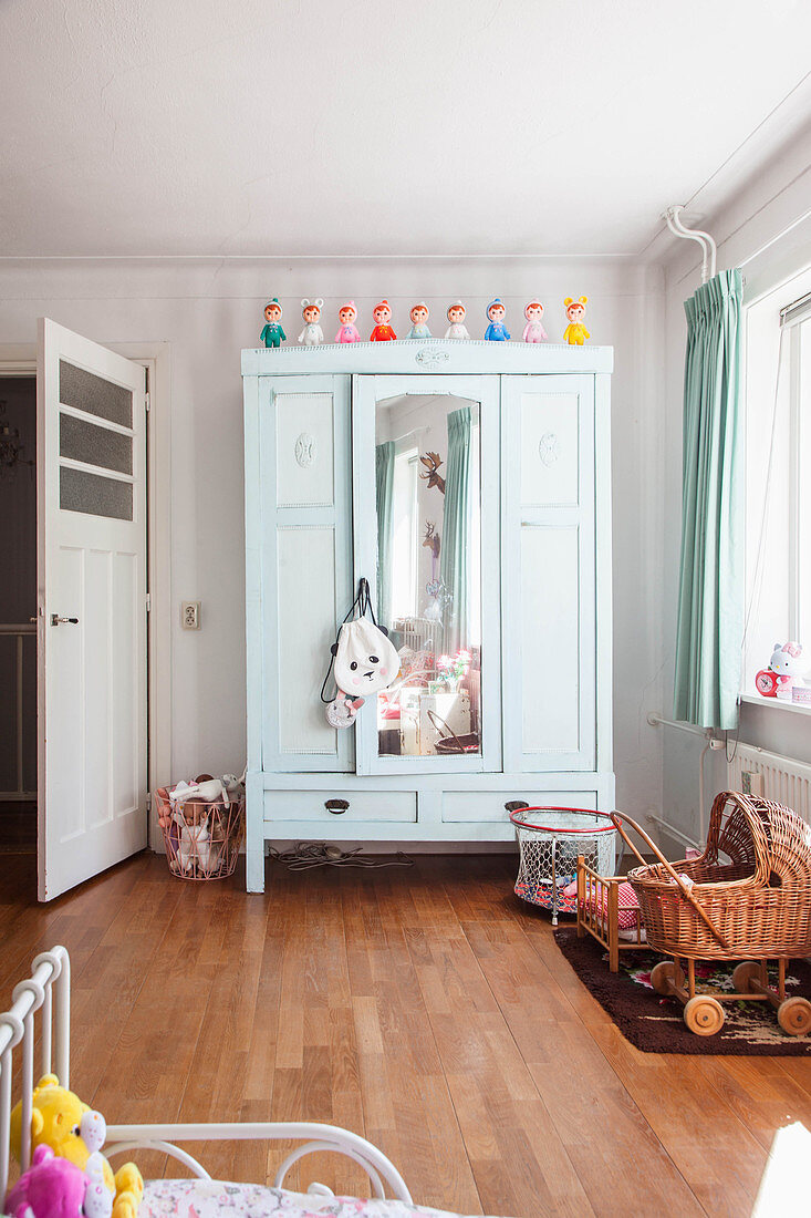 Mint-green wardrobe with mirrored door and wicker dolls' pram in girl's bedroom