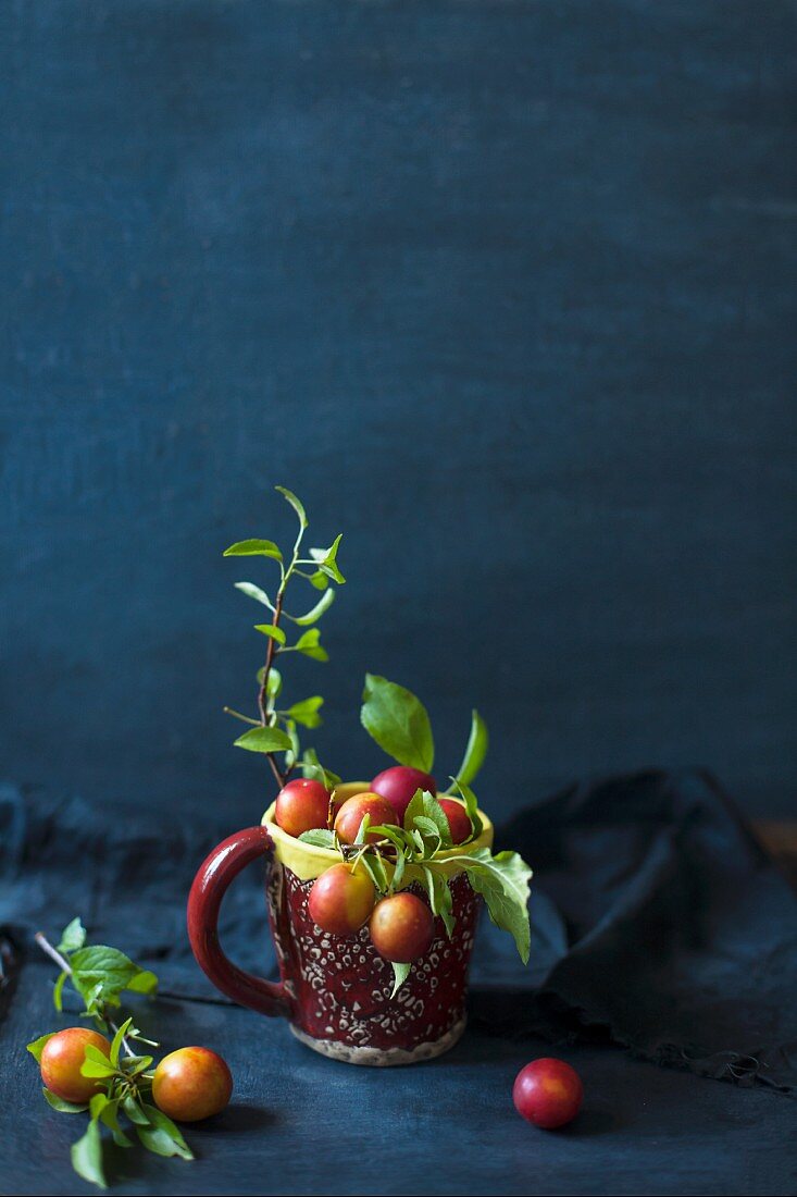 Small plums and leaves in a cup