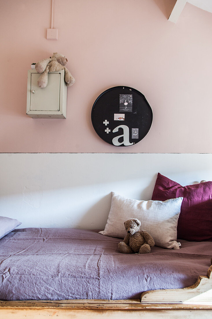 Cushions and teddy on child's bed in girl's bedroom with pink and white wall