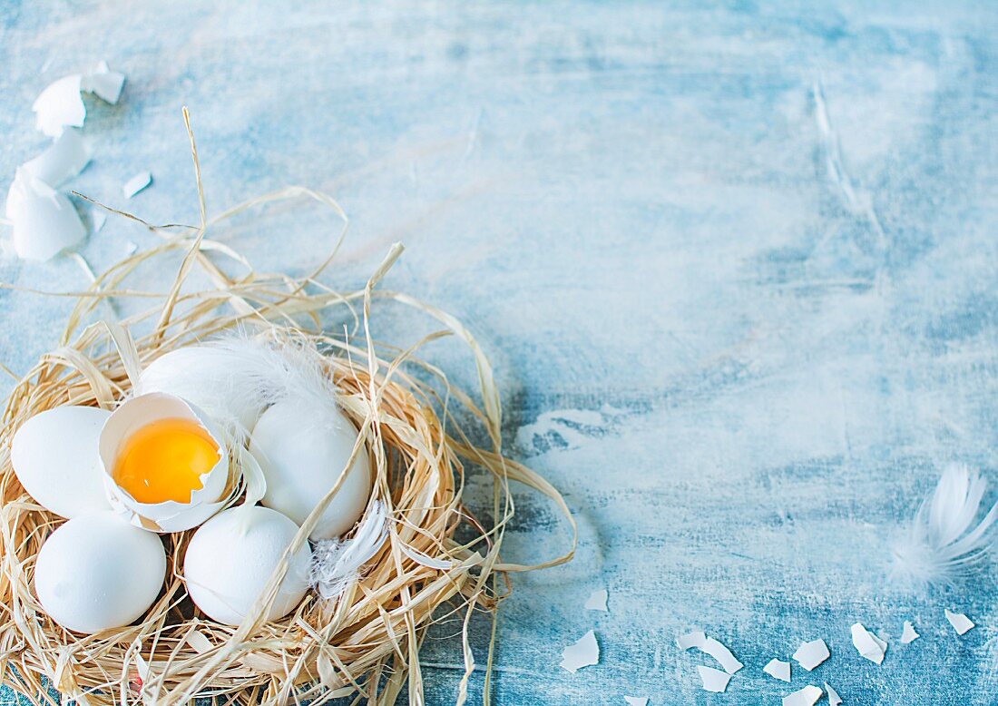 White eggs, whole and cracked open, in a straw nest