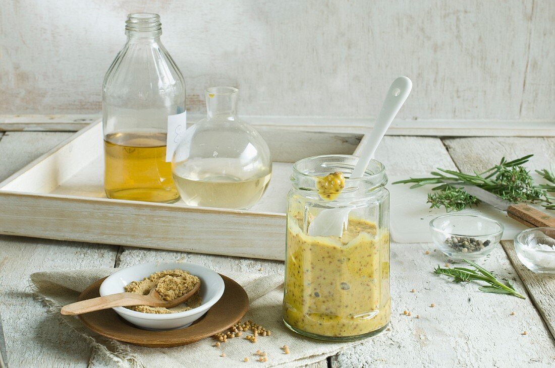 Homemade mustard in a jar with a spoon and the ingredients behind it