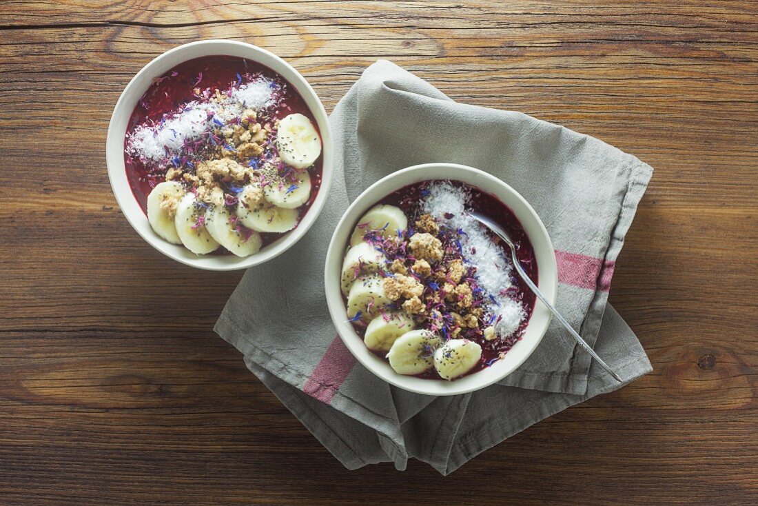 Rote Smoothie Bowls mit Chiasamen und Essblüten auf Holzuntergrund