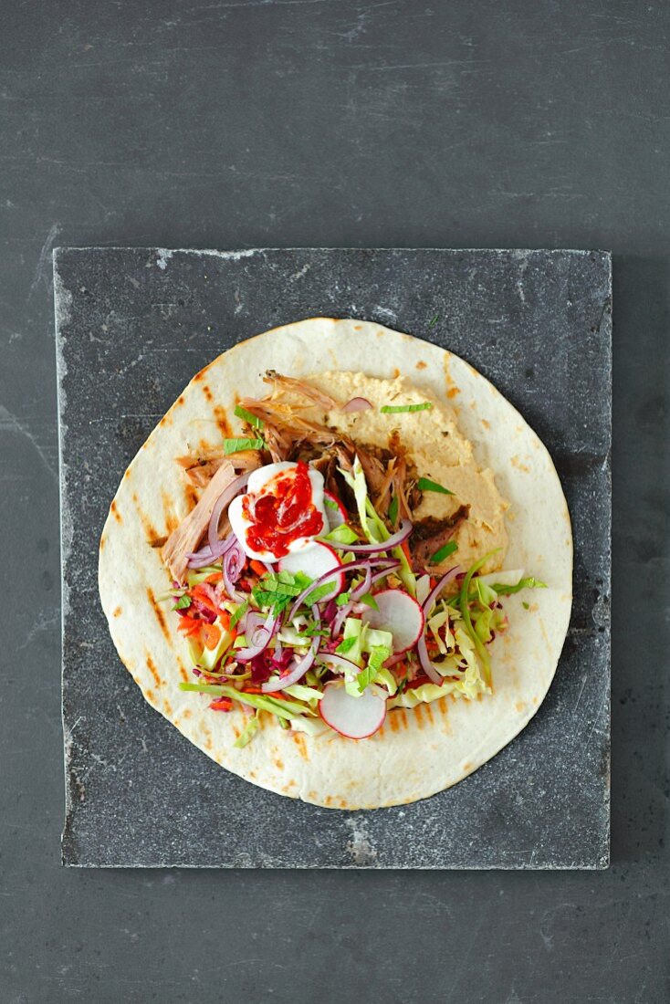 A tortilla wrap with pulled pork, hummus and coleslaw