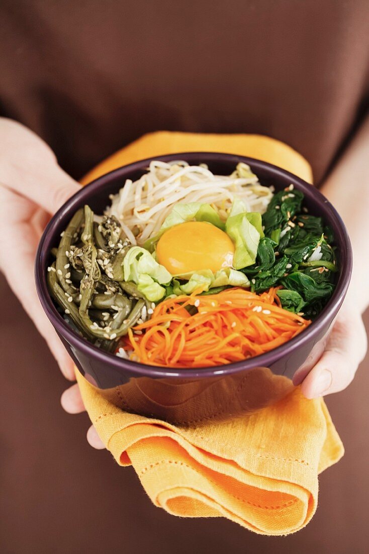 A person holding a bowl of bibimbap (rice dish from Korea)